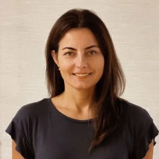 Smiling woman with shoulder-length dark hair wearing a dark gray top, against a neutral background.