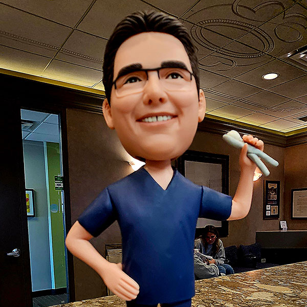 Oversized caricature statue of a smiling dentist in blue scrubs holding a tooth model in a lobby.