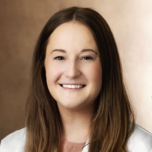 Portrait of a smiling young woman with long brown hair against a warm beige background.